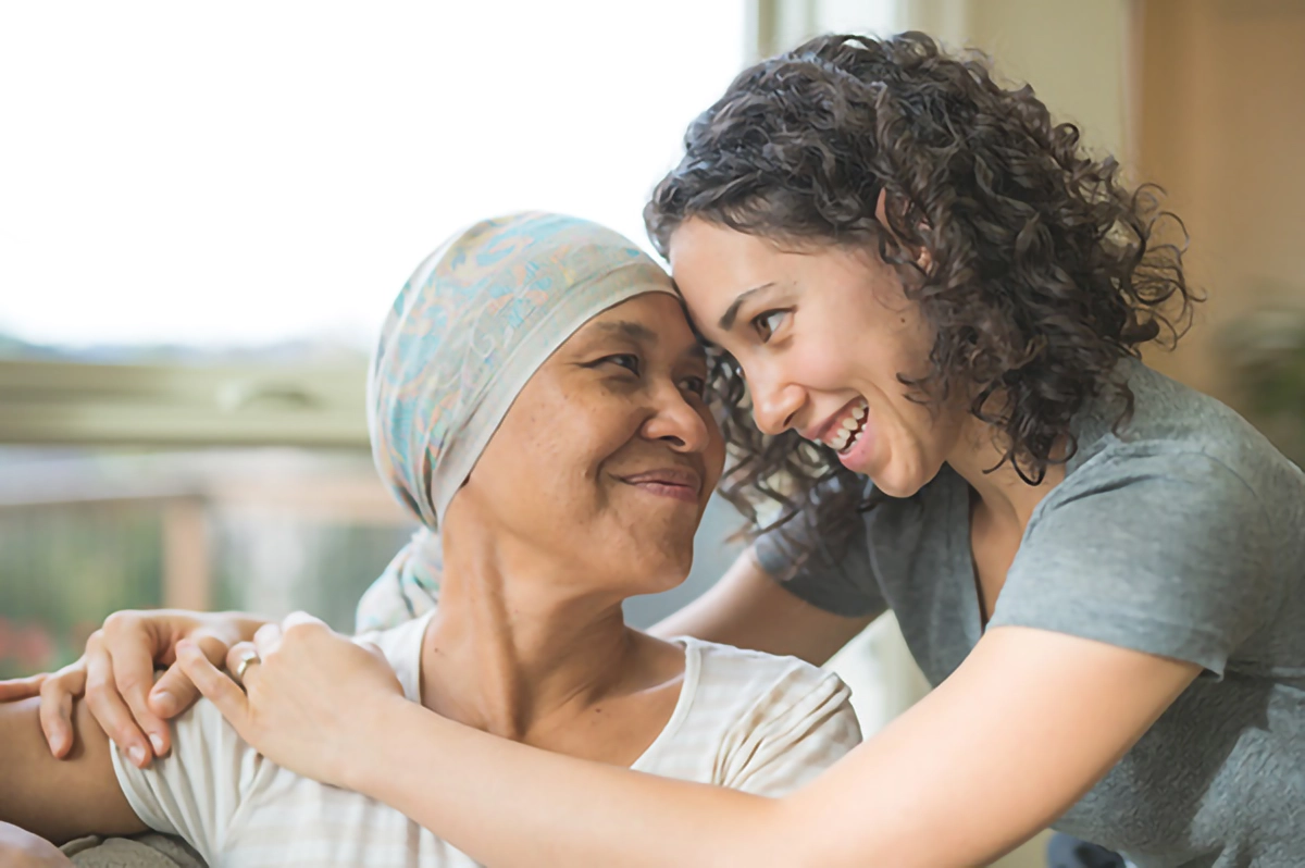 Image shows two women hugging. One has cancer and the other is offering support.